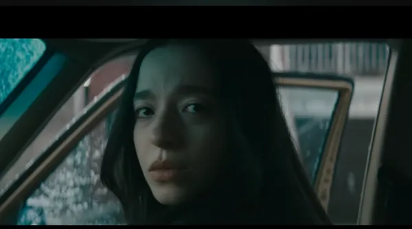 A contemplative individual looks back out of a car.