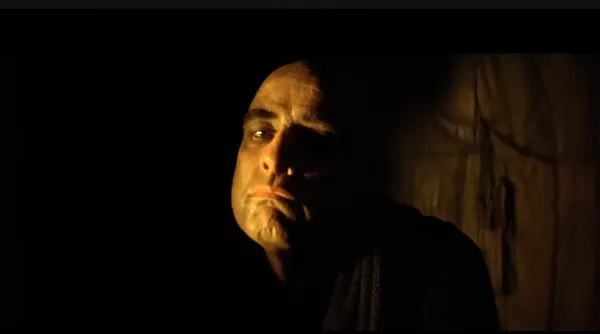 A dimly lit, intense close-up portrait of a character.