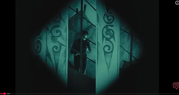 A mysterious figure is peering through abstract, patterned walls.