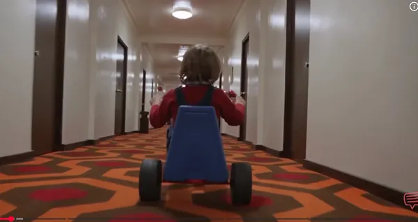 Child riding a tricycle down a long hotel corridor.