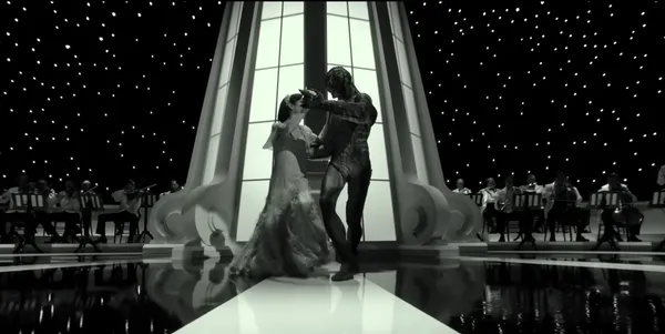 A couple dances elegantly in front of an orchestra with a starry background.
