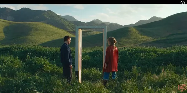 Two people stand facing a doorway in a vast, open landscape.