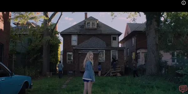 A girl stands in front of an old house in a suburban neighborhood.
