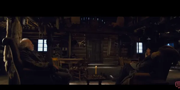 Two characters are sitting in a dimly lit cabin with a candle and chessboard.