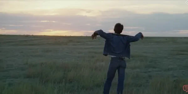 A person standing in a field with arms outstretched towards the sunset.