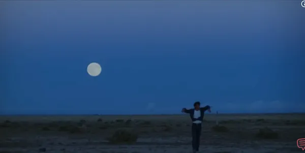 A solitary figure walks across an open landscape under a full moon.