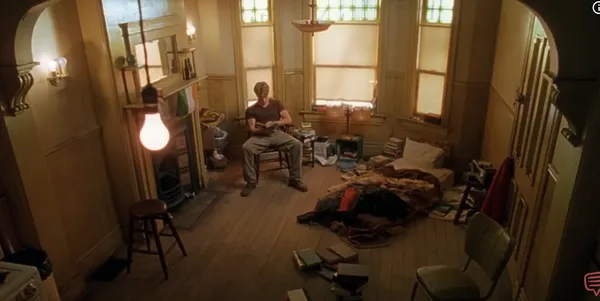 A person sits in a cluttered room reading a book.