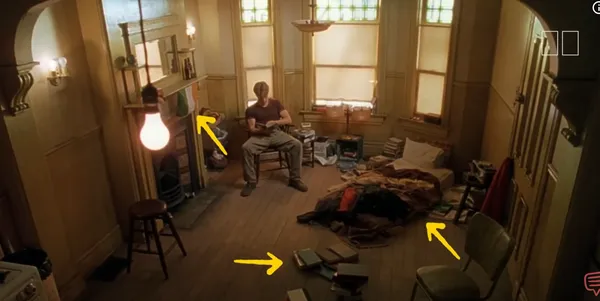 A person sitting in a cluttered room with books and a bed on the floor.