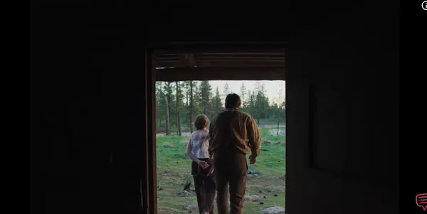 A couple walks out into a lush, forested landscape through a doorway.