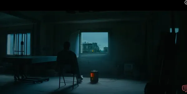 A person sits alone in a dimly lit room facing a window.