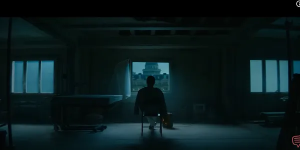 A lone figure sits in a dimly lit room facing a window with a city view.