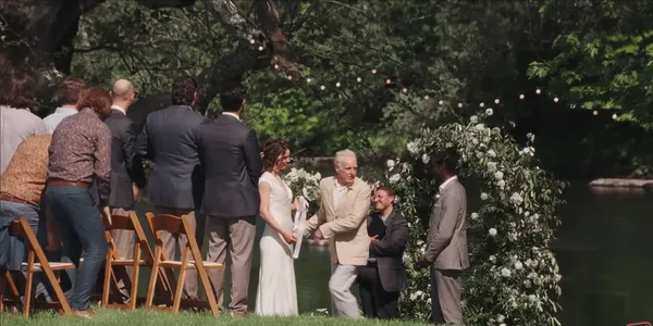 An outdoor wedding ceremony by a river with guests and a couple at the altar.