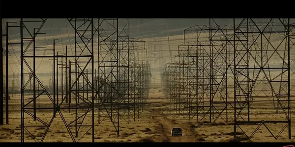 A car driving through a field of power lines in a vast landscape.