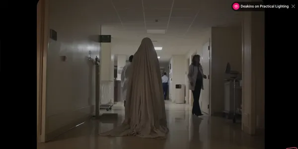 A mysterious figure draped in a sheet stands in a hospital hallway.