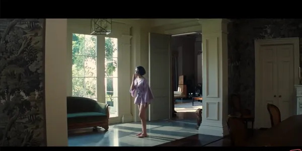 A person stands in a sunlit room looking out a window.