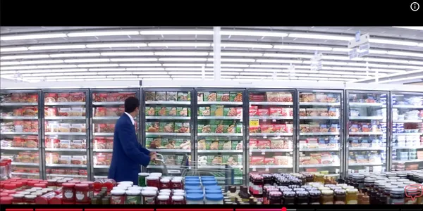 A person shopping in a supermarket aisle with frozen goods.