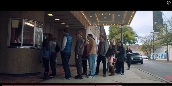 People lined up outside a ticket booth on a street.