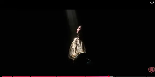 A person is dramatically illuminated by a single beam of light in a dark setting.