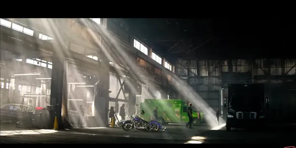 Sunbeams illuminate an industrial garage with vehicles and people.