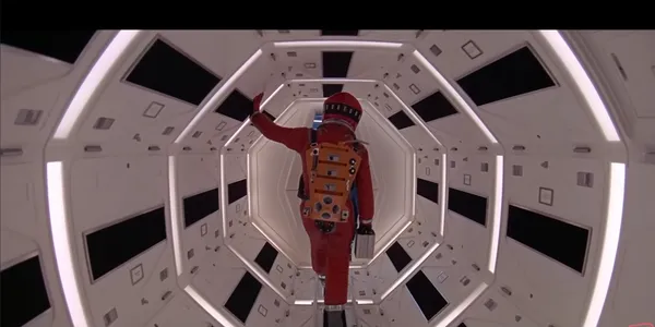 Astronaut walking through a futuristic, well-lit spacecraft corridor.