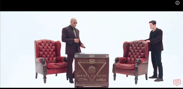 Two men standing by a vintage television and red chairs in a white void