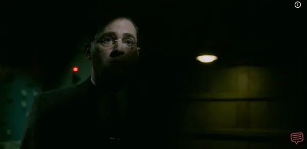 A man in glasses looking intently towards a dim light source in the dark