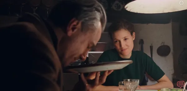 A woman watching quietly as a man examines a dish of food closely