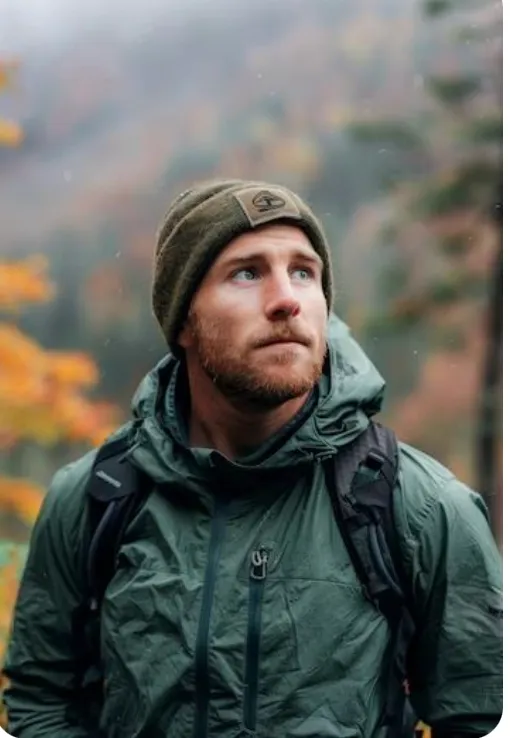 A man in outdoor gear gazes thoughtfully amidst an autumnal forest background.