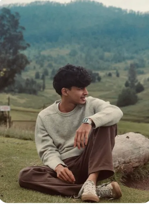 Person sitting on grass with a scenic mountain background.