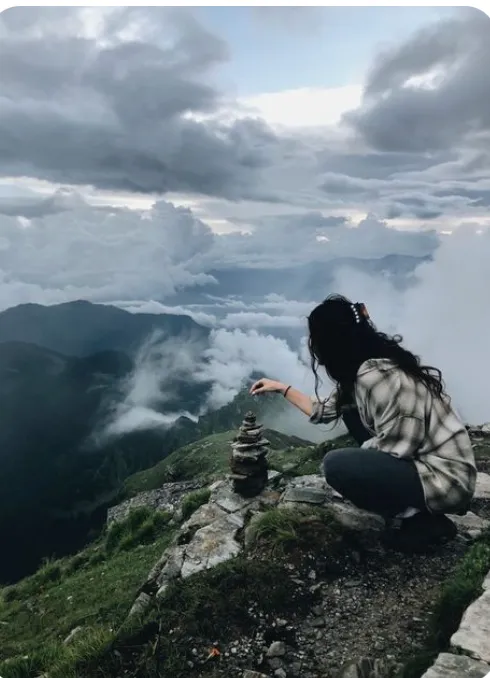 A person stacking rocks on a mountain with a dramatic cloudy sky.