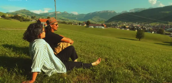 Two people relaxing in a scenic grassy hillside with mountains in the background.