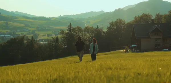 Two people walking in a picturesque grassy landscape with hills in the background.