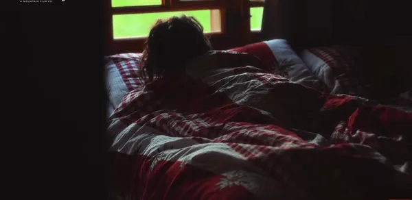 A person lying in bed looking towards a window.
