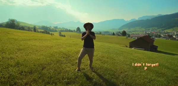 Person standing in a sunlit field with mountains in the background