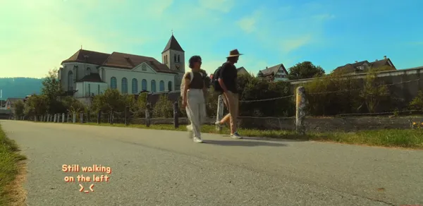 Two people walking along a rural road with a church in the background.