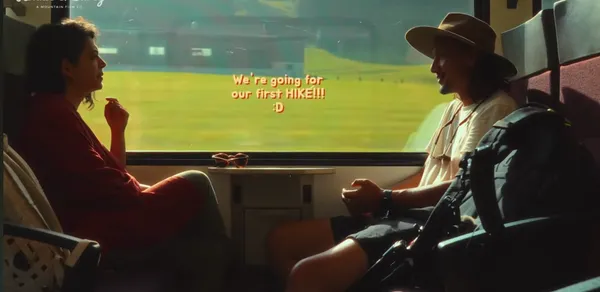 Two people sitting and talking on a train with a scenic view outside.