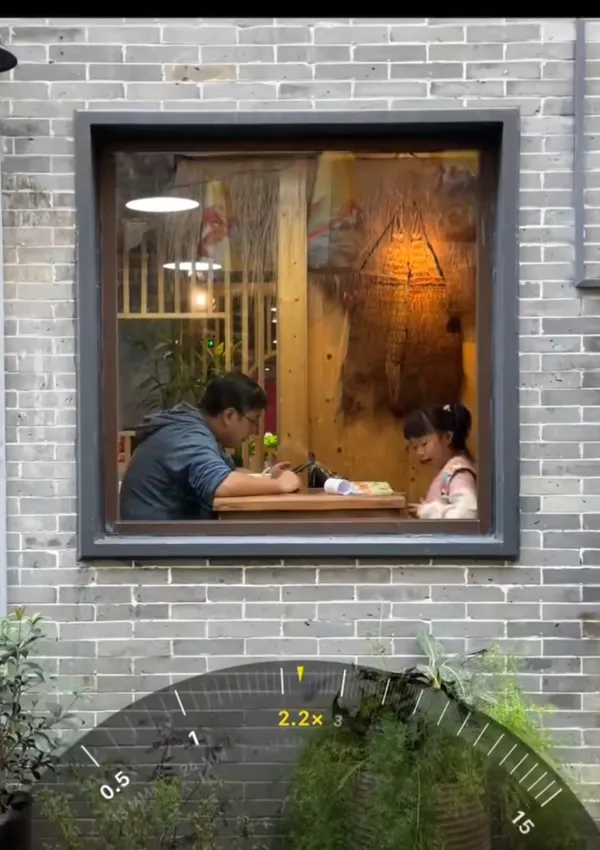 A man and child are seen dining through a window.