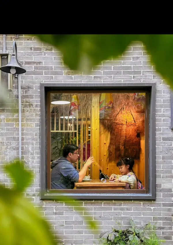 A parent and child share a moment inside a cozy cafe as seen through a window.