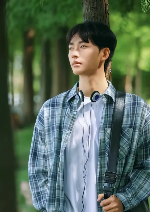A young person thoughtfully gazing while standing against a tree.