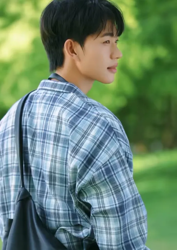 A person in a plaid shirt outdoors with a blurred green background.