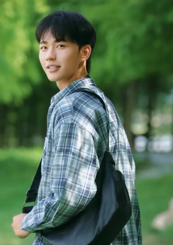 A person turning and smiling in a green outdoor setting.