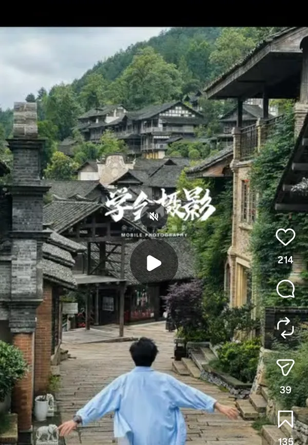 Person walking towards traditional village buildings surrounded by greenery.